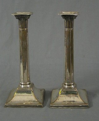 A pair of 19th Century silver candlesticks with Corinthian capitals and bead work borders, raised on square bases,