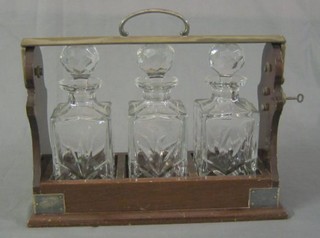 An Edwardian mahogany and silver plated tantalus frame containing 3 later cut glass spirit decanters