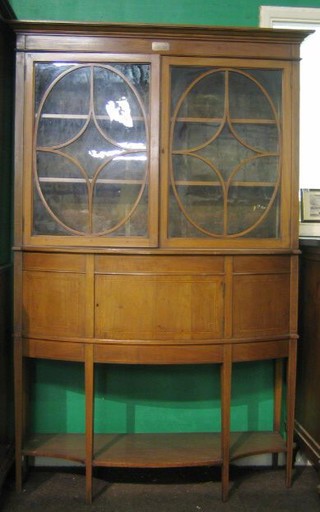 An Edwardian Sheraton style inlaid mahogany display cabinet on cabinet, the upper section with moulded cornice and adjustable shelves, enclosed by astragal glazed panelled doors, the base of bow front form fitted a drawer, raised on square tapering supports with undertier 46"