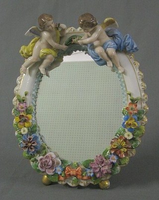 A 19th Century oval plate mirror contained in a Meissen style floral encrusted frame, surmounted by a figure of cherubs 11"