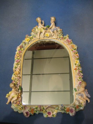 A Dresden style arch shaped plate mirror contained in a floral encrusted frame surmounted by 2 cherubs