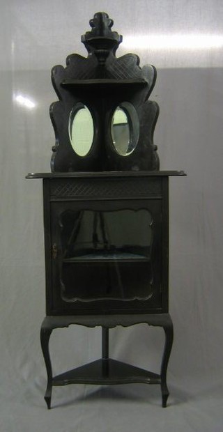 An  Edwardian ebonised corner cabinet with raised back, the base fitted a cupboard enclosed by a glazed panelled door, raised on cabriole supports 26"