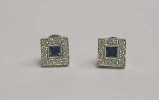 A pair of ear studs set square cut sapphires surrounded by 13 diamonds