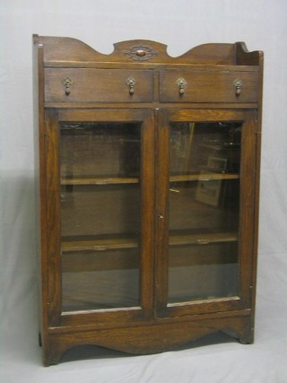 A 1930's oak bookcase the top with tree quarter gallery fitted 2 drawers above a double cupboard enclosed by glazed panelled doors, raised on bracket feet 36"