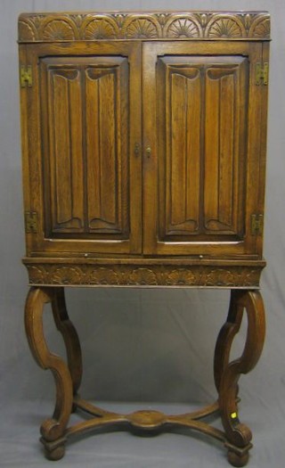A Tudor style carved oak cocktail cabinet with arcaded decoration enclosed by linen fold panelled doors, the base fitted a brushing slide, raised on cabriole supports united by a Y shaped stretcher 30"