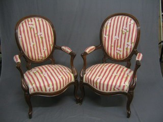 A pair of Victorian rosewood show frame open arm chairs upholstered in floral material, raised on French cabriole supports ending in brass castors