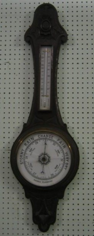 An Edwardian aneroid barometer and thermometer contained in a  carved oak wheel case (glass cracked)