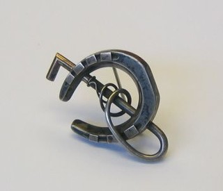 A silver and inlaid gold brooch in the form of a riding crop and horse shoe