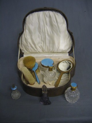 A gilt enamel 10 piece dressing table set comprising 2 hand brushes, 2 clothes brushes (1f), hand mirror, 3 dressing table jars, perfume atomiser and a glass scent bottle, contained in a shaped case