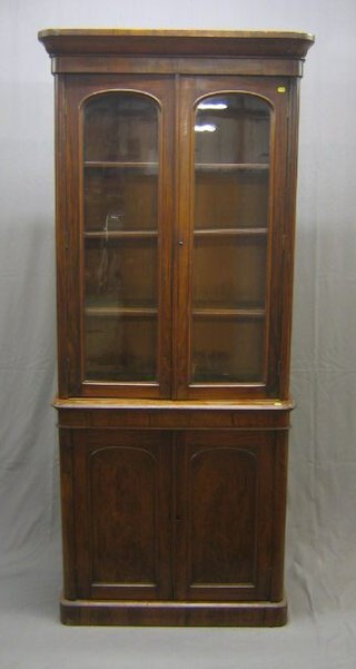A Victorian rosewood bookcase on cabinet, the upper section with moulded cornice, fitted adjustable shelves enclosed by arched panelled doors, the base fitted a cupboard, raised on a platform base 36"