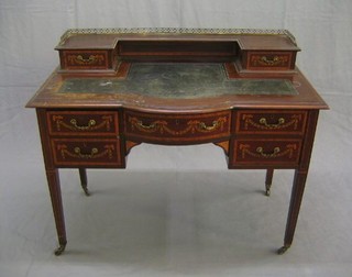 An Edwardian bow front inlaid mahogany writing table, the inverted break front upper section with pierced brass three- quarter gallery fitted 2 drawers and with inset tooled writing surface, the base with 1 long and 4 short drawers, raised on square tapering supports ending in brass caps and castors, 42"