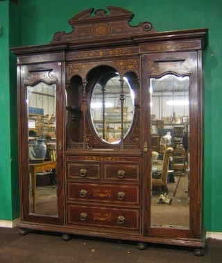 A Maples & Co handsome Victorian inlaid mahogany wardrobe, the moulded cornice with raised pediment, the centre section fitted a niche backed by an oval plate mirror above 2 short and 2 long drawers, flanked by a pair of cupboards enclosed by arched bevelled plate mirrored doors, raised on bun feet, heavily inlaid throughout, 65"