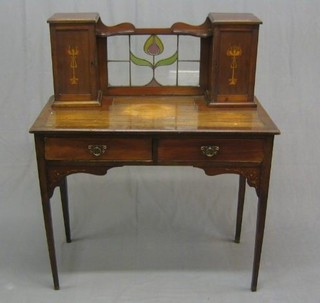 An Art Nouveau inlaid mahogany writing table, the raised back with lead glass panel to the centre flanked by a pair of cupboards enclosed by inlaid panelled doors, the base inset a writing surface above 2 short drawers, raised on square tapering supports 36"