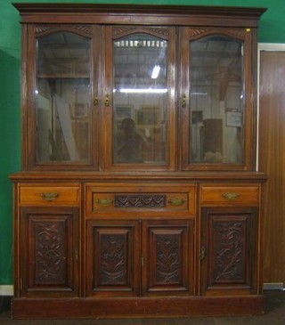 An Edwardian carved walnutwood secretaire bookcase, the upper triple section with moulded cornice, the interior fitted adjustable shelves enclosed by arched panelled doors, the base fitted secretaire drawer above triple cupboard flanked by a pair of doors, raised on a platform base 70"