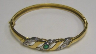 A lady's 18ct yellow gold bangle set an oval cut emerald surrounded by diamonds