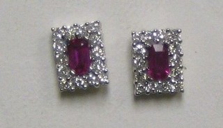 A pair of lady's white gold ear studs set rectangular cut rubies surrounded by 16 diamonds