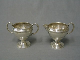 An American Sterling silver twin handled sugar bowl and matching cream jug with embossed decoration, raised on spreading feet