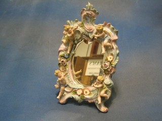 A shaped plate easel mirror contained in a Continental porcelain frame decorated cherubs (f and r)