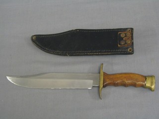 A reproduction Bowie knife with 8 1/2" blade and wooden grip, contained in a black leather scabbard (some damage to blade)