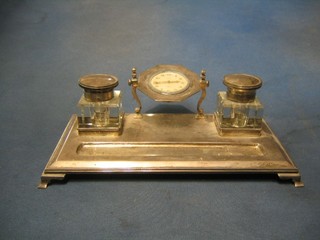 A silver standish, the centre fitted an 8 day clock flanked by a pair of square cut glass inkwells complete with liners and silver collars, the base fitted a pen receptical fitted on ogee bracket feet 11" Birmingham 1928