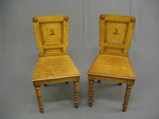 A pair of 19th Century honey oak hall chairs, the backs with painted armorial decoration and solid seats, raised on ring turned supports