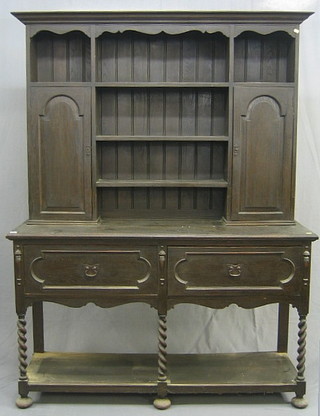 An Art Nouveau dark oak dresser, the raised back fitted shelves and cupboards, the base fitted 2 long drawers, raised on spiral turned supports with potboard, 60"
