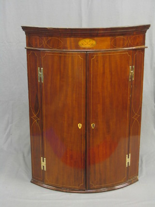 An inlaid Georgian mahogany bow front corner cabinet the interior fitted shelves enclosed by panelled doors inlaid by satinwood stringing, 31"