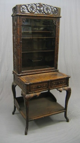 A 19th/20th Century Oriental Padouk wood cabinet with pierced pediment, the interior fitted shelves enclosed by  glazed panelled doors, the base fitted a writing surface above 2 short drawers, with undertier, raised on cabriole supports 27"