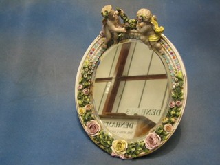 An oval bevelled plate mirror contained in a Dresden porcelain frame with floral encrusted decoration surmounted by figures of cherubs 12" (silvering going on mirror)