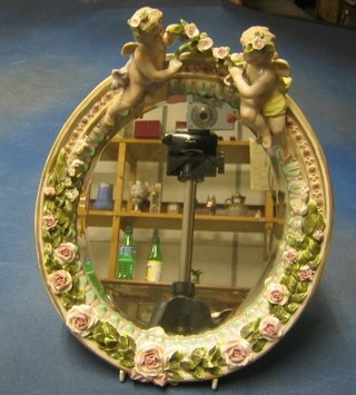 A 19th Century oval plate mirror contained in a porcelain encrusted frame surmounted by 2 cherubs (some chips)