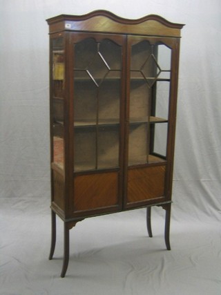 An Edwardian shaped mahogany display cabinet with double dome top, the interior fitted shelves enclosed by astragal glazed panelled door (1 panel f), raised on splayed supports 34"