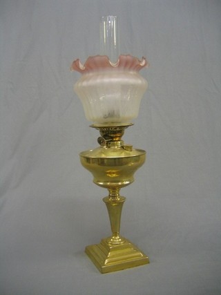 A 19th Century brass oil lamp reservoir raised on a circular spreading foot with stepped base and pink glass shade