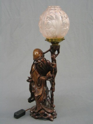 An Eastern carved root wood figure of a standing sage converted to an electric table lamp with pink glass shade 15"