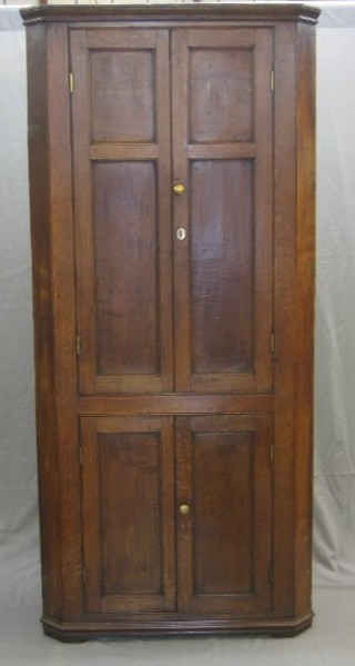 An 18th/19th Century oak double corner cabinet with moulded cornice, the upper section fitted shelves enclosed by panelled doors, the base fitted shelves enclosed by a panelled door, 37"