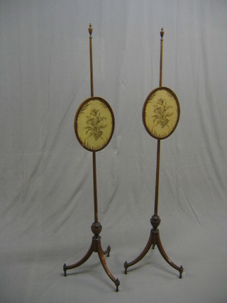 A pair of 19th Century mahogany pole screens with urn finials and oval wool work banners, raised on pillar and tripod supports