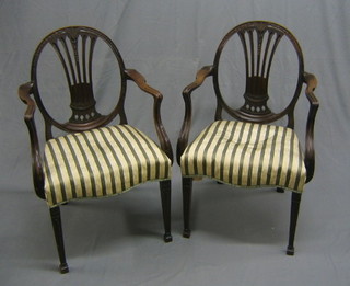 A pair of 19th Century Hepplewhite style open arm carver chairs with pierced vase splat backs, seats upholstered in Regency stripe (1 with old break to back) raised on square tapering supports ending in spade feet