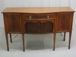 An Edwardian Georgian style mahogany sideboard of serpentine outline with crossbanded top and satinwood stringing, fitted 1 long drawers above a cupboard enclosed by tambour shutter, flanked by a pair of cupboards, raised on square tapering supports ending in spade feet (recently repolished)
