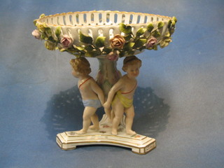 A circular 19th/20th Century Continental pierced porcelain table centre piece with basket work rim and floral encrusted decoration, supported by 3 cherubs, the base with crown shield mark 9"