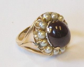 A 9ct gold dress ring set an oval cabouchon red stone supported by demi-pearls