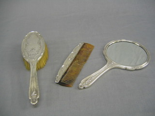 An embossed silver 3 piece dressing table set comprising hand mirror, hair brush and comb with floral decoration, Birmingham 1911 (some holes)