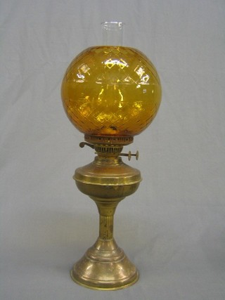 A brass oil lamp reservoir raised on a reeded column with amber glass shade and clear glass chimney