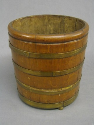 A circular coopered oak barrel with brass banding, raised on 3 brass bun feet 9"