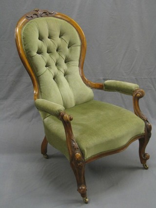 A Victorian carved walnut show frame spoon back open arm chair upholstered in green buttoned material, raised on carved cabriole supports
