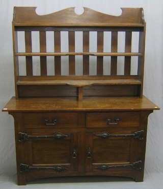 A Voisey style Art Nouveau oak dresser with raised slatted back fitted 3 shelves, the base fitted 2 drawers above a double cupboard with forged iron handles and hinges 60" (some old worm holes to the raised back)