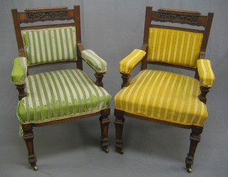 A pair of Edwardian carved walnut open arm chairs raised on square tapering supports ending in brass caps and castors