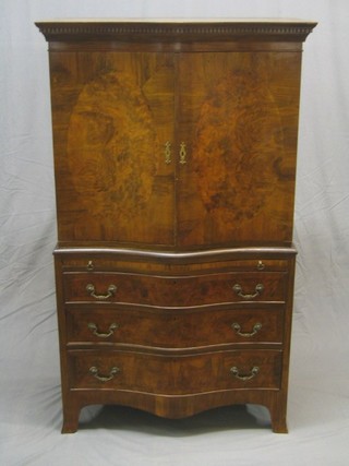 A Georgian style serpentine fronted cabinet on chest, the upper section with moulded and dentil cornice the interior fitted adjustable shelves enclosed by panelled doors, the base fitted a brushing slide above 3 long drawers on swept bracket feet, 36"