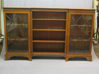 A handsome satinwood and crossbanded inverted break front bookcase, the centre section with open adjustable shelves flanked by a pair of cupboards enclosed by astragal glazed panelled doors, raised on splayed bracket feet 79"