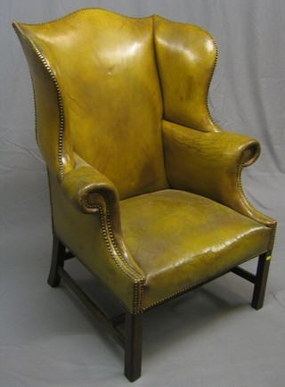A Georgian style wing armchair upholstered in green leather, raised on square supports