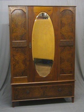 A 1920's figured walnut wardrobe enclosed by an oval bevelled plate mirror panelled door, the base fitted a drawer 48"
