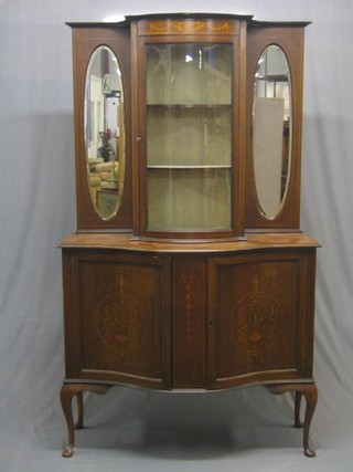 An Edwardian inlaid mahogany sideboard/display cabinet of serpentine outline, the upper section fitted a bow front display cabinet the interior fitted adjustable shelves flanked by a pair of oval panelled mirrors, the base fitted a cupboard enclosed by a pair of panelled doors, raised on cabriole supports 48"